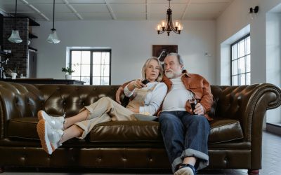 Ein Pärchen mittleren Alters sitzt auf einer Couch und guckt Fernsehen